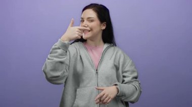 Gri kapüşonlu, gülümseyen esmer kadın elleri mor arka planda, pozitiflik ve yaratıcılık saçıyor..