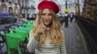 Kırmızı bereli ve gözlüklü sarışın genç bir gezgin şehir manzarasını incelerken bir kadın meşgul sokağı işaret etmek için parmağını kullanıyor..