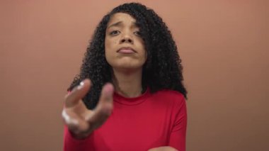 Kadın el hareketleriyle para isterken stüdyoda şeftali arkaplanı ile eli açık kırmızı bluz giyer; çaresizlik.