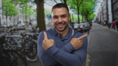 Gülümseyen İspanyol adam şehir caddesinde park halindeki bisiklet ve arabaların yanında işaret parmağıyla işaret ediyor..