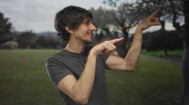 Yeşil ormandaki ağaca işaret eden gri tişörtlü genç adam merak keşfi.