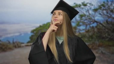 Mezuniyet kepi ve cübbesi takan kadın, doğa arka planıyla gelecek olasılıkları ve başarıları simgeliyor..