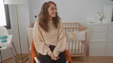 Sıcak bir yatak odasında beşikle gülümseyen, yumuşak bir kazak giyen, bebek odası mobilyalarıyla çevrili, sıcak ve evcimen bir hava saçan bir kadın..