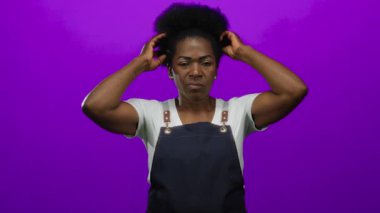 Saçı kapalı gözlerle ayarlayan, mor arka plana karşı önlük giyen sakin bir duyguyu resmeden ve basit güzelliğe odaklanan bir kadın..