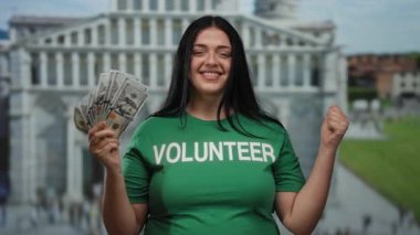 İşeme kulesinin önünde yeşil gönüllü tişörtü giymiş bir kadın bize açık havada gülümseyen bir dolar tutuyor..