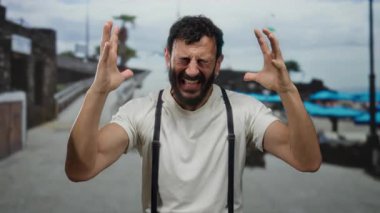 Hispanik sakallı bir adam duygusal olarak deniz kenarında bir gezinti yapıyor. Arka planda deniz ve deniz var..