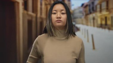 Şehir sokaklarında genç bir kadın açık şehir ortamında dikkatli bir jest yapıyor, dikkat çekici bir ifade ve odaklanma sergiliyor, özellikle el hareketi ve vücut dili üzerinde duruyor..