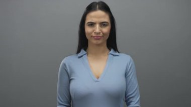 Mavi gömlekli İspanyol kadın gri duvara karşı kameraya doğru hareketler yapıyor. Kendine güvenen bir bakışla, bir bağlantı ve nişan anı yakalıyor..