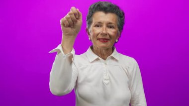 Kıdemli kadın, parlak mor bir arka planda el kol hareketi yapıyor, beyaz bir gömlek giyiyor, çeşitli duyguları ifade ediyor, iletişim ve özen göstermeyi öneriyor..