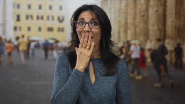 Orta yaşlı kadın, bulanık turist kalabalığının ortasında güneşli eski kasaba sokağında el yordamıyla ağzını kapatıyor; sessizlik.