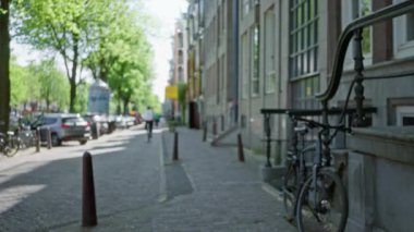 Amsterdam 'da bulanık bir şehir manzarası. Ağaç kaplı bir sokak, park edilmiş bisikletler ve sakin bir şehir manzarası yaratan tarihi mimari..