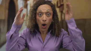 Ağzı açık bir kadın elleriyle başını tutuyor ve taştan kemer yolu ile eski kasaba sokağında kendine sarılıyor; sürpriz sevinç.