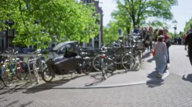 Güneşli bir günde insanların, ağaçların ve park halindeki bisikletlerin bulanık arkaplanlarında bisiklet süren bir adam..