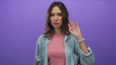 Pembe gömlekli ve mavi ceketli bir kadın, izole edilmiş mor arka planda arkadaşça bir hareket sergiliyor..