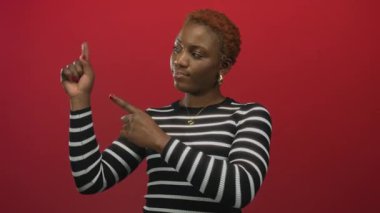 Çizgili süveterli altın halkalı küpeler takan genç bir kadın canlı kırmızı stüdyoda parmak kola; şüphecilik.