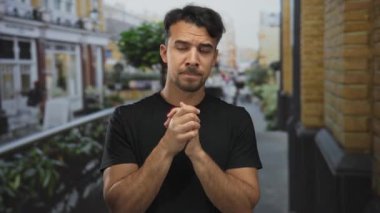 Şehrin sokaklarında gezen Latin kökenli genç adam, derin düşünce ya da sinirsel beklenti içeren hareketli bir şehir ortamında ellerini sıkarak dalgın görünüyor..