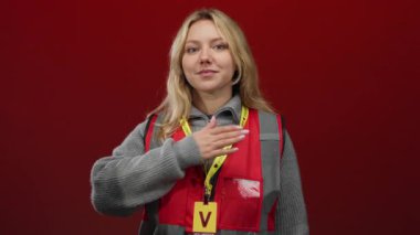 Kırmızı arka planda kırmızı yelek giyen, kendine güvenen ve gururlu bir kadın..