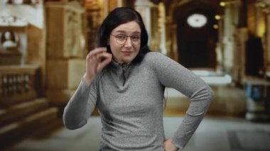 Katolik kilisesi ortamında gözlüklü bir kadın, günlük gri bir süveter giyiyor ve süs dekoruna karşı güvenle duruyor, meraklı bir ifadeyi yakalıyor..