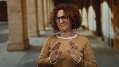 Eski bir üniversite ortamında İspanyol orta yaşlı bir kadın açık havada reddedilme hareketi yapıyor. Antik mimariye karşı duyguları ve mirası yakalıyor, gözlük takıyor..