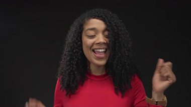 Kadın uzun kıvırcık saçlarını savurur ve her iki elini de dinamik stüdyo dansında gülümseyen yüzüyle kaldırır; mutluluk..