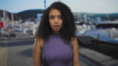 Sahil limanında, arka planda açık gökyüzünün altında kayık ve tepelerle şaşırmış bir kadın..