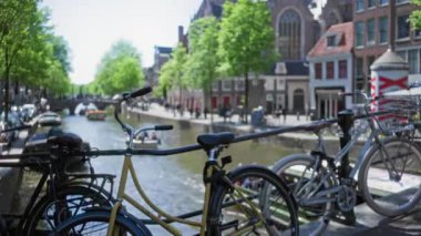 Güneşli bir gökyüzünün altındaki bulanık arka planda tekneli, yemyeşil ağaçlı ve tarihi mimarili manzaralı amfi kanallara bakan bir köprüde odaksız bisikletler..