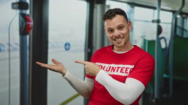 Kırmızı tişörtlü genç adam otobüsün içinde gülümserken elleri açık, sıradan ve davetkar bir atmosferi yakalıyor.