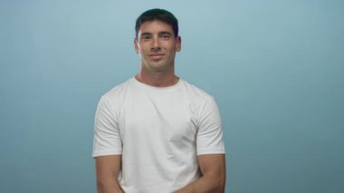 Açık mavi bir stüdyoda beyaz t-shirt giyen bir adam gözlerinin üzerine el dürbünü yapıyor..