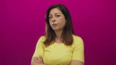 Orta yaşlı, sarı kollu, kolları çapraz sarı bir kadın. Eflatun bir stüdyoda çıplak kollarını gösteriyor..