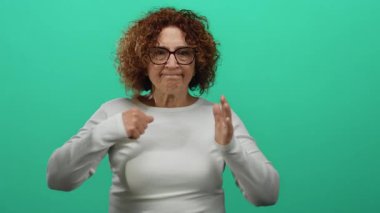 Orta yaşlı esmer, kıvırcık saçlı, ispanyol bir kadın. Kavgalı bir poz veriyor. Avuç içinde, izole edilmiş yeşil arka plana karşı..