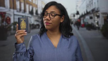 Gündüz gözlüklü bir kadın Kanada pasaportunu tutuyor ve şehir sokaklarında yan yan bakıyor. Gurur kimliği..