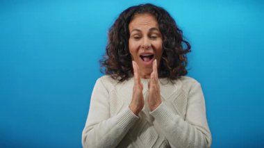 Kıvırcık saçlı, sıcacık kazaklı, parlak mavi arka planda gülümseyen bir kadın..