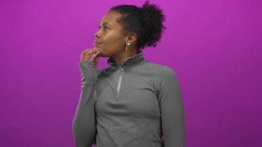 Gri fermuarlı, çenesinde parmağı olan ve mor stüdyoda büzüşmüş dudakları olan bir kadın..