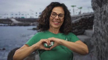Sahilde gönüllü tişört giyip, ellerle gülen bir kadın doğadaki toplum ruhunu gözler önüne seriyor..