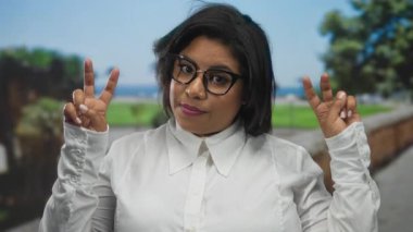 Parkta, beyaz gömlekli, canlı, bulanık yeşil gözlüklü, sıradan, Latin, İspanyol tarzı, güneşli ve dost canlısı bir ortama karşı jestler yapan bir kadın..