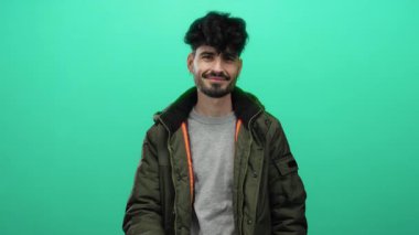 Genç adam, izole edilmiş yeşil bir arka plana karşı gizemli bir jest yapıyor, bir gizem ve entrika anı yakalıyor..