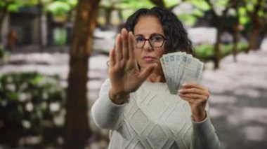 Mısırlı orta yaşlı bir kadın, elinde Mısır sterliniyle bir şehir caddesinde açık hava banknotları tutuyor. Duraklama hareketi yapıyor, finansal sorunları vurguluyor ve açık şehir ortamını vurguluyor..