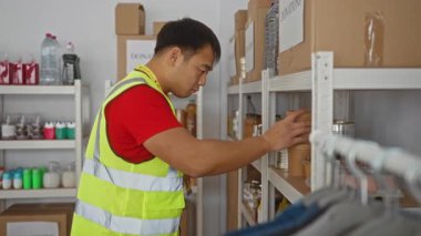 Yardım merkezinde çalışan genç adam, dağıtım ve yönetim için kaydedilen öğelere odaklanarak yüksek görünürlüklü yelek giyen bağışları organize ediyor.