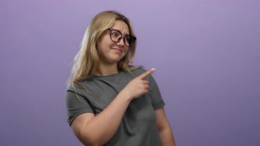 İki eli de izole edilmiş mor arka planı olan, gözlüklü, gri gömlekli, sarı saçlı, modern yaşam tarzında sorgulayıcı bir tavır sergileyen bir kadın..