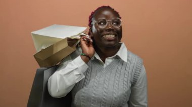 Kahverengi arka planda alışveriş torbaları tutan bir kadın, neşeli ve hayat dolu bir sahne yaratarak, alışverişin neşe ve memnuniyetini yansıtıyor.