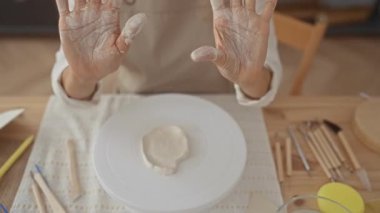Kadın çömlek atölyesinde çamurla kaplı elleri gösteriyor; yaratıcılık işçiliği odaklı özveri.