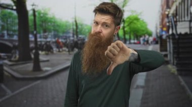 Uzun sakallı adam, bisiklet ve sokak lambalarının arasında, şehir caddesinde baş parmak hareketi gösteriyor; hoşnutsuzluk.