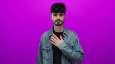 Genç İspanyol bir adam, izole edilmiş pembe arka plana el kaldırarak içten ve sakin bir tavırla söz veriyor..