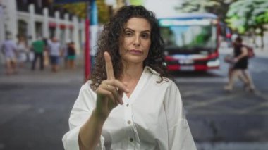 Ciddi yüzü olan beyaz gömlekli İspanyol kadın yoğun caddede kamerayı işaret ediyor..