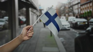Şehir caddesinde finiş bayrağı taşıyan adam, binalar ve trafik ile açık hava atmosferinde ulusal gururunu sergiliyor..