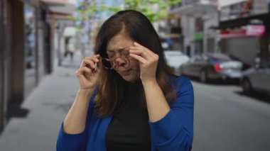 Kadın, mavi ceket ve gözlük takan, stres yorgunluğu çeken şehir merkezindeki caddelerde tapınak basıyor..