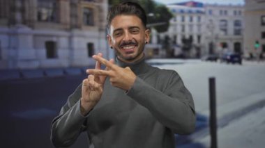 Kentsel caddede elleri ile hashtag işareti gösteren genç İspanyol adam gri kazak giyiyor; sosyal bağlantı.