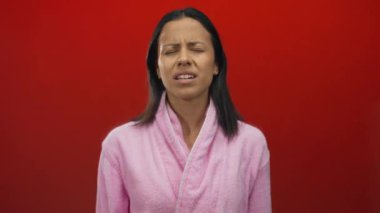 Pembe bornozlu kadın, dışlanmış kırmızı bir arka plan duvarına karşı hayal kırıklığına uğramış görünüyor..