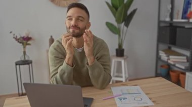 Oturma odasında dizüstü bilgisayarla oturan genç adam içeride çalışırken düşünceli görünüyor.