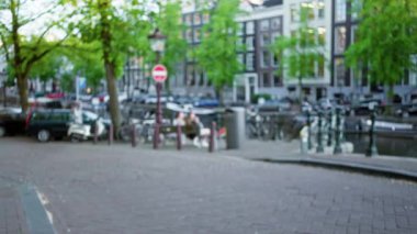 Amsterdam 'ın bulanık şehir manzarası, kentsel bir kanal, yeşil ağaçlar ve park edilmiş bisikletler, büyüleyici sokak manzarası ve sakin atmosferi vurguluyor..
